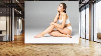 Young beautiful woman with perfect body in white underwear sitting on the floor isolated on white background Wall mural